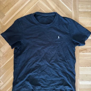 Svart t-shirt från Ralph Lauren - Klassisk svart t-shirt från Ralph Lauren med liten broderad logga på bröstet. T-shirten har rund halsringning och korta ärmar, perfekt till jeans eller shorts. Tillverkad i mjuk bomull för skön känsla hela dagen.