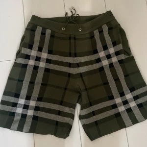 Olivgröna rutiga shorts Burberry M - Snygga olivgröna shorts från Burberry med klassiskt rutigt mönster i svart och vitt. Modellen har snörning i midjan och är tillverkad i mjukt material som känns skönt mot huden. Perfekta för dig som vill ha en stilren och trendig look.