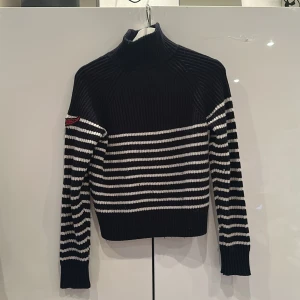 Svart och vit randig stickad tröja från Zadig & Voltaire - Snygg svart och vit randig stickad tröja från Zadig & Voltaire med hög krage. Tröjan har långa ärmar och ett broderat ZADIG &VOLTAIRE mätke i rött på ena ärmen. Perfekt för kyligare dagar. Tröjan är knappt andvänd och säljer för jag växt ut den ❣️❤️💕