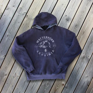 Mörkblå hoodie med tryck från Alperna  - Säljer en mörkblå hoodie med tryck av Matterhorn Cervinia på framsidan. Tröjan har inget märke då den är köpt i Alperna som souvenir. Den är använd men är i bra skick, det framhäver bara elegansen i plagget. Färgen kan variera lite beroende på ljus, vilket du kan se på de olika bilderna. Perfekt för en sval sommar kväll eller att bära till havs! 