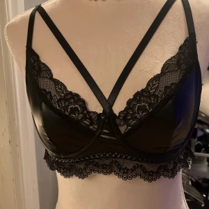 Svart spetsdetaljerad topp - Svarta spetsdetaljer och justerbara axelband. Perfekt för en elegant look med en touch av glamour. Den har en vacker spetskant och en glansig finish som ger en lyxig känsla. Nyskick 