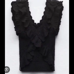 Svart spetsblus med volanger - Snygg svart blus i spets med volangdetaljer. Den är ärmlös och har en v-ringad design som ger en elegant look. Perfekt för att lyfta vilken outfit som helst.