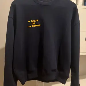 Snygg och stilren sweatshirt i mörkblå färg med gult tryck på bröstet där det står “D’ONCE DE LA SENSE”. Tröjan har en avslappnad passform med rund halsringning, ribbade muddar och nederkant. Mjuk och bekväm bomullskvalitet – perfekt för vardagsbruk eller en chill outfit.  Storlek: XS Skick: Väldigt bra – knappt använd, inga fläckar eller skador. Pris: 400kr Märke: D’ ONCE DE LA SENSE 