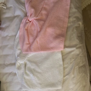 Rosa och vit tubtopp - Två tubtoppar, en i ljusrosa och en i vit. Perfekta för varma dagar med sin enkla och stilrena design. De har en ribbad textur som ger en fin detalj och är stretchiga för en bekväm passform.