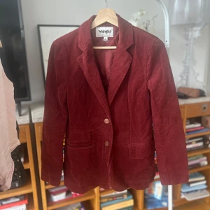 Vinröd manchesterkavaj från Wrangler - Säljer en snygg vinröd kavaj i manchester från Wrangler. Kavajen har en klassisk design med två knappar framtill och långa ärmar. Perfekt för att ge en stilren touch till din outfit. Passar bra till både vardag och speciella tillfällen.