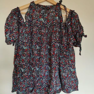 Blommig klänning från Mavi - Charmig blommig klänning från Mavi i mörkblått med röda och vita blommor. Klänningen har korta ärmar med knytband och en luftig passform. Perfekt för en somrig look!