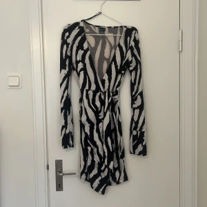 Svart och vit omlottklänning - Snygg svart och vit omlottklänning med zebramönster. Klänningen har långa ärmar och en v-ringad design. Perfekt för en trendig look.