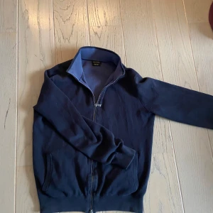 Mörkblå tröja med dragkedja från Massimo Dutti - Snygg mörkblå tröja från Massimo Dutti med dragkedja framtill. Tröjan har en hög krage och långa ärmar, perfekt för kyligare dagar. Den är tillverkad i ett mjukt material som ger en bekväm passform.