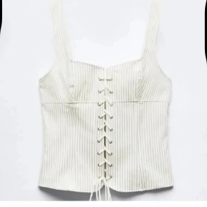Randig korsett från Zara - Snygg randig korsett från Zara i beige och vit med snörning framtill. Perfekt för att ge en stilren och chic look. Den har breda axelband och en figurnära passform. Aldrig använd