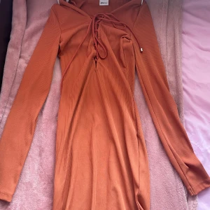 Orange ribbad klänning från Gina Tricot - Snygg orange ribbad klänning från Gina Tricot med långa ärmar och snörning framtill. Perfekt för en stilren look med en touch av färg. Klänningen har en figurnära passform och är tillverkad i ett mjukt material.