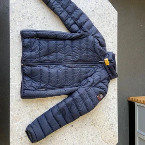 Mörkblå dunjacka från Parajumpers - Säljer en snygg mörkblå dunjacka från Parajumpers med en cool patch på ärmen. Jackan har en dragkedja och är quiltad för extra värme. Perfekt för kyliga dagar! Har även ett litet håll på armen (finns inget kvitto) pris kan diskuteras 