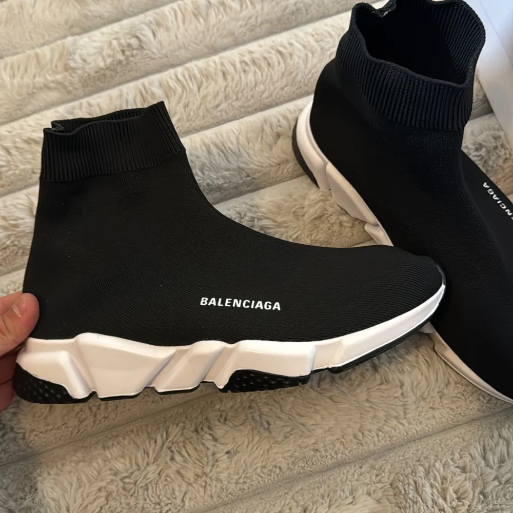 Snygga svarta sneakers från Balenciaga med en strumpliknande design och vit sula. Skorna har en modern och stilren look med Balenciaga-loggan på sidan. Perfekta för en trendig och bekväm stil.. Kengät.