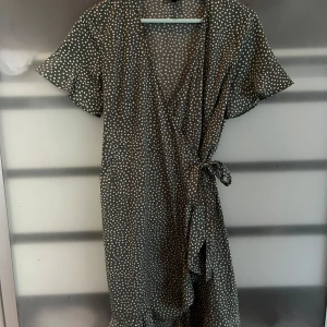 Grön prickig klänning  - Säljer en  grön klänning med vita prickar från Vero Moda. Klänningen har korta ärmar och en omlott-design med knytning runt midjan. Storlek M. Används 2-3 gånger 