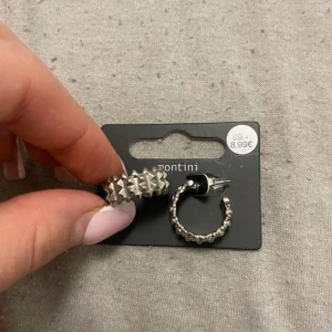 Silvriga örhängen från Montini - Snygga silvriga örhängen från Montini med ett unikt designmönster av små pyramidformade nitar. Perfekta för att ge en edgy touch till din outfit. De är runda och har en bekväm stängning.