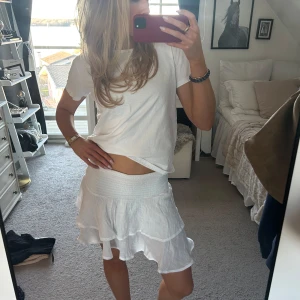 Vit volangkjol - Säljer en söt vit kortkjol med volanger. Perfekt för sommardagar och har en elastisk midja för extra komfort. Kjolen är luftig och lätt, vilket gör den idealisk för varma dagar.