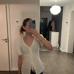 Vit topp från BikBok - Säljer en mycket söt vit topp från BikBok i storlek XS. Toppen har korta puffärmar och en v-ringad design med knytning framtill. Perfekt för en stilren look!