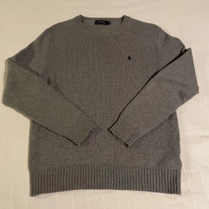 Grå stickad tröja från Polo Ralph Lauren - Säljer en stilren grå stickad tröja från Polo Ralph Lauren med broderad logga på bröstet. Ny pris ca 2400kr. Tröjan har långa ärmar och ribbade muddar vid ärmslut och nederkant. Perfekt för en klassisk och bekväm look.