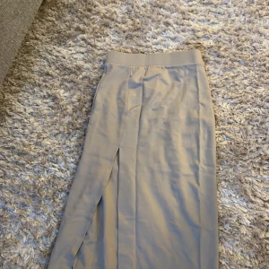 Beige långkjol från Bik Bok - Snygg beige långkjol från Bik Bok med en stilren design. Kjolen har en diskret slits framtill som ger en elegant touch. Perfekt för en chic och avslappnad look.