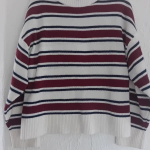 Stickad tröja - Säljer en snygg randig tröja i vinrött, vitt och marinblått. Tröjan har långa ärmar och en rund halsringning. Perfekt för kyligare dagar!