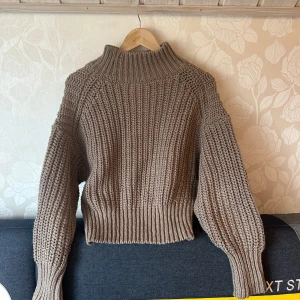 Brun stickad tröja från H&M - Säljer en mysig brun stickad tröja från H&M. Tröjan har en hög krage och långa ärmar med ribbade muddar. Perfekt för kyliga dagar.