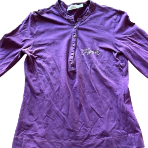 Lila långärmad topp - Lila långärmad topp med glittrig text på bröstet! Knapparna går att öppna och stänga så man kan välja hur man vill ha den!💕En liten defekt som på vänster arm som borde gå att laga. Priset kan alltid diskuteras. Skriv om frågor finns!💕