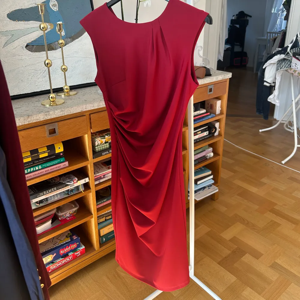 Elegant röd klänning från Rinascimento med draperad detalj på sidan. Klänningen har en smickrande passform och är ärmlös, perfekt för en stilren look. Tillverkad i Italien. Storlek 38 men passar även 36.. Mekot.