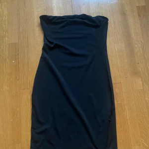 Svart axelbandslös klänning - Snygg svart axelbandslös klänning perfekt för en kväll ute. Den har en elegant och enkel design som framhäver figuren. Passar bra till både klackar och sneakers beroende på stil.