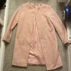 Rosa kappa från Gina Tricot - Säljer en söt rosa kappa från Gina Tricot i storlek 34. Den har en rund halsringning och stängs med knappar framtill. Perfekt för vår och höst!