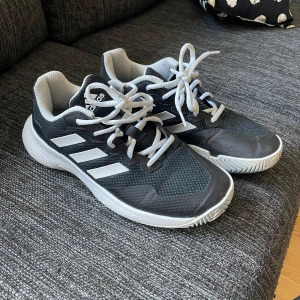 Adidas Gamecourt 2 - Säljer ett par Adidas Gamecourt 2 sneakers i svart och vitt. Skorna har en stilren design med de klassiska tre ränderna på sidan och snörning framtill. Perfekta för padel eller vardagsbruk.