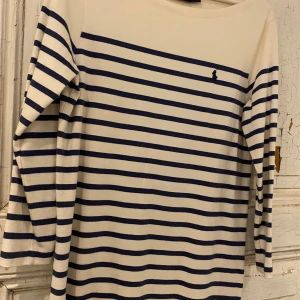 Randig tunika/klänning  från Polo Ralph Lauren stl M  - Säljer en stilren randig tunika/klänning  från Polo Ralph Lauren i vitt och blått. Tröjan har långa ärmar och ett klassiskt broderat märke på bröstet. Perfekt för en avslappnad och snygg look.