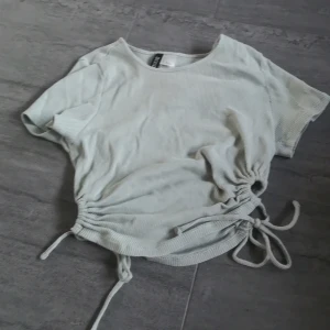 Grön ribbad topp från H&M Divided - Säljer en snygg grön ribbad topp från H&M Divided. Toppen har korta ärmar och knytning i sidorna för en justerbar passform. Perfekt för en avslappnad stil!