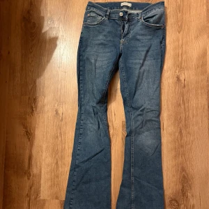 Blå bootcut jeans - Snygga blå bootcut jeans med klassisk femficksdesign och knappgylf. Perfekta för en avslappnad stil. Passar bra till både sneakers och klackar.
