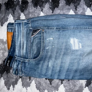 Blå jeans från Replay - Snygga blå jeans från Replay med slitna detaljer och klassisk femficksdesign. De har en normal passform och är perfekta för en avslappnad stil. Märkeslogga på baksidan av midjan. Riktigt snygga jeans i mycket bra skick!🤩