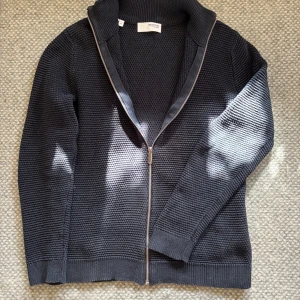 Svart stickad kofta med dragkedja - Säljer en stilren svart stickad full zip kofta från Selected Homme. Den har långa ärmar och en ribbad struktur som ger en klassisk look. Använd fåtal gånger och inga defekter |storlek S| Nypris:699kr|