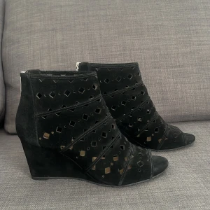 Svarta kilklackade boots från Michael Kors - Snygga svarta boots med kilklack från Michael Kors för damer. Storlek 40, och väldigt bra kvalitet. Nypris omkring 1000-1700 kronor. Måste bara borstas och putsas litegrann för att de ska se helt rena ut. Skorna har ett unikt mönster med utskärningar och en dragkedja bak för enkel påtagning. Perfekta för att ge en stilfull touch till din outfit