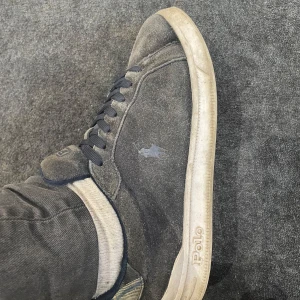 Marin blåa sneakers från Ralph Lauren 38 - Snygga svarta sneakers från Ralph Lauren med klassisk design. Skorna har en diskret logga på sidan och snörning framtill. Sulan är vit och ger en stilren kontrast. Perfekta för en avslappnad look. Dem är lite slitna i sulan inuti där av priset men funkar fint om man byter sula sen är dem lite smutsiga men enkelt att göra rent 