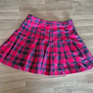 Rutig kjol från H&M Divided - Snygg rutig kjol i rött och svart från H&M Divided. Kjolen har en dragkedja i sidan och ett klassiskt rutmönster som ger en tidlös look. Perfekt för att addera lite färg till din garderob! Storlek 38