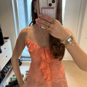 Volang topp  - Säljer en snygg orange/rosa blus med volangdetaljer framtill. 💞Blusen har smala axelband som är justerbara och ett lätt mönster💞toppen är något genomskinlig💞. Perfekt för varma dagar! Inga defekter ! Skriv vid frågor 💞passar både XS o S