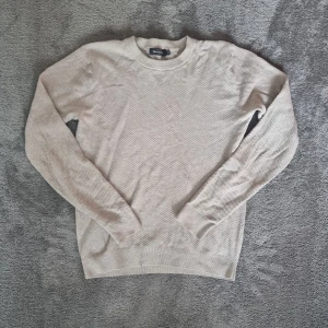 Beige stickad tröja från Dressmann - Säljer en stilren beige stickad tröja från Dressmann. Tröjan har en rund halsringning och långa ärmar, perfekt för kyligare dagar. 
