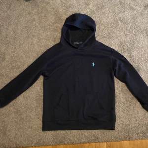 Mörkblå hoodie från Ralph Lauren - Säljer en snygg mörkblå hoodie från Ralph Lauren med den klassiska loggan på bröstet. Tröjan är tillverkad i 100% bomull och har en praktisk magficka. Perfekt för en avslappnad stil.