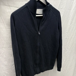 Marinblå kofta från Bernhardt - Snygg marinblå kofta från Bernhardt med dragkedja och ribbad krage. Perfekt för en stilren look. Passar bra över en skjorta för en mer formell stil. Textilfiber, annars bra skick 