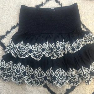 Svart kjol med broderade detaljer - Snygg svart kortkjol med elastisk midja och vackra vita broderade detaljer. Perfekt för att ge en stilfull touch till din outfit. 