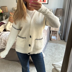 Vit kofta med broderinh - Säljer en söt vit kofta från Miss Selfridge med svarta broderade detaljer vid fickorna och ärmarna. Koftan har en ribbad struktur och knäpps med stora knappar framtill!