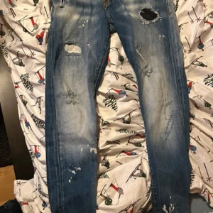 Blå jeans från Dsquared2 *kan diskutera pris* - Säljer ett par blå jeans från Dsquared2 med slitna detaljer och hål för en cool look. Jeansen har en slim passform och är tillverkade i Italien. Perfekta för dig som vill ha en edgy stil.