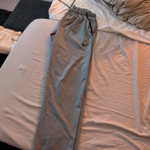 Grå träningsbyxor från Nike - Säljer ett par grå träningsbyxor från Nike med elastisk midja och sidofickor. Perfekta för träning eller en avslappnad dag. Byxorna har en diskret Nike-logga på benet.