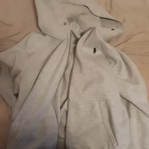 Grå hoodie från Ralph Lauren - Säljer en stilren grå hoodie från Ralph Lauren med det klassiska logotypen på bröstet. Hoodien har en dragkedja och praktiska fickor framtill. Perfekt för en avslappnad look. Öppen för snabba affärer. Möts upp upp helst i Stockholm. Vill inte skambud så kom med rimliga seriösa priser. Ska se om jag kan fixa hålet som är ända felet annars är den i använda men fint skick. Annars kan man nog fixa det med någon som kan sy igenom.