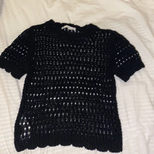 Svart stickad topp från MNG - Säljer en svart stickad topp från mango. Den har ett öppet stickmönster och korta ärmar, perfekt för lager-på-lager eller som statement-plagg. Tillverkad i Turkiet. Passar bra till både jeans och kjol. 🖤