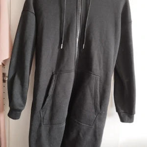 Svart hoodie med dragkedja och huva - Svart hoodie med hel dragkedja framtill, huva med snörning och stora fickor på magen. Tröjan har långa ärmar och är tillverkad i mjukt material som känns skönt mot huden. Perfekt för en avslappnad och chill stil.Kan hämtas upp i Malmö 