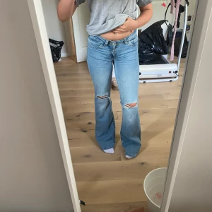 Bootcut jeans från Nelly med slitningar - Ljusblå bootcut jeans från Nelly med slitna knän och snygga detaljer på bakfickorna. Klassisk femficksmodell i jeansmaterial med låg midja och vida ben. Perfekta för en avslappnad och trendig look. Aldrig använda