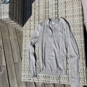 Ljusgrå ribbad tröja från NA-KD - Säljer en ljusgrå ribbad långärmad tröja från NA-KD med half zip och rund halsringning. Tröjan är i stickad bomullsmix och har en snygg metallring på dragkedjan. 
